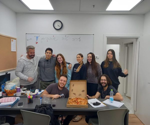 8 חברי הסגל בכיתה מסביב למגש פיצה